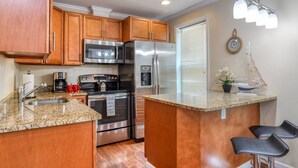 A kitchen with wooden cabinets, stainless steel appliances, granite countertops, a built-in oven, a refrigerator, a coffee maker, and a small island with bar stools. - Blue Moon Suite (St. Augustine)