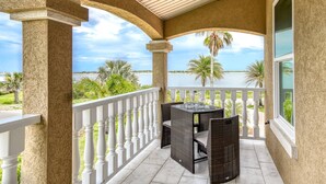 A covered balcony with a table and chairs, overlooking a body of water and palm trees. - Dolphin Bay Apartment (St. Augustine)