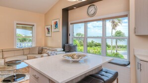 A modern kitchen with a large island, a dining area with a glass table, and a view of the outdoors. - Dolphin Bay Apartment (St. Augustine)