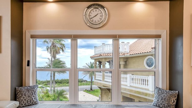 A room with a large window, a wall clock, and a seating area with cushions. - Dolphin Bay Apartment (St. Augustine)