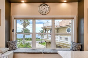 Una habitación con un ventanal grande, un reloj de pared y una zona de estar con cojines.