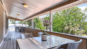 Un patio cubierto con mesa y sillas, ventanas amplias y vistas a árboles y edificios.