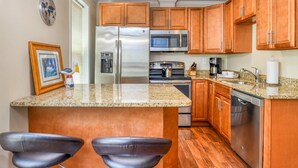 Una cocina con gabinetes de madera, electrodomésticos de acero inoxidable, encimeras de granito y dos taburetes de cuero.