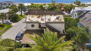 A two-story house with a patio overlooking the beach, featuring a sunburst design on the wall, a covered outdoor seating area, and a view of the ocean. - Castillo del Sol (St. Augustine)