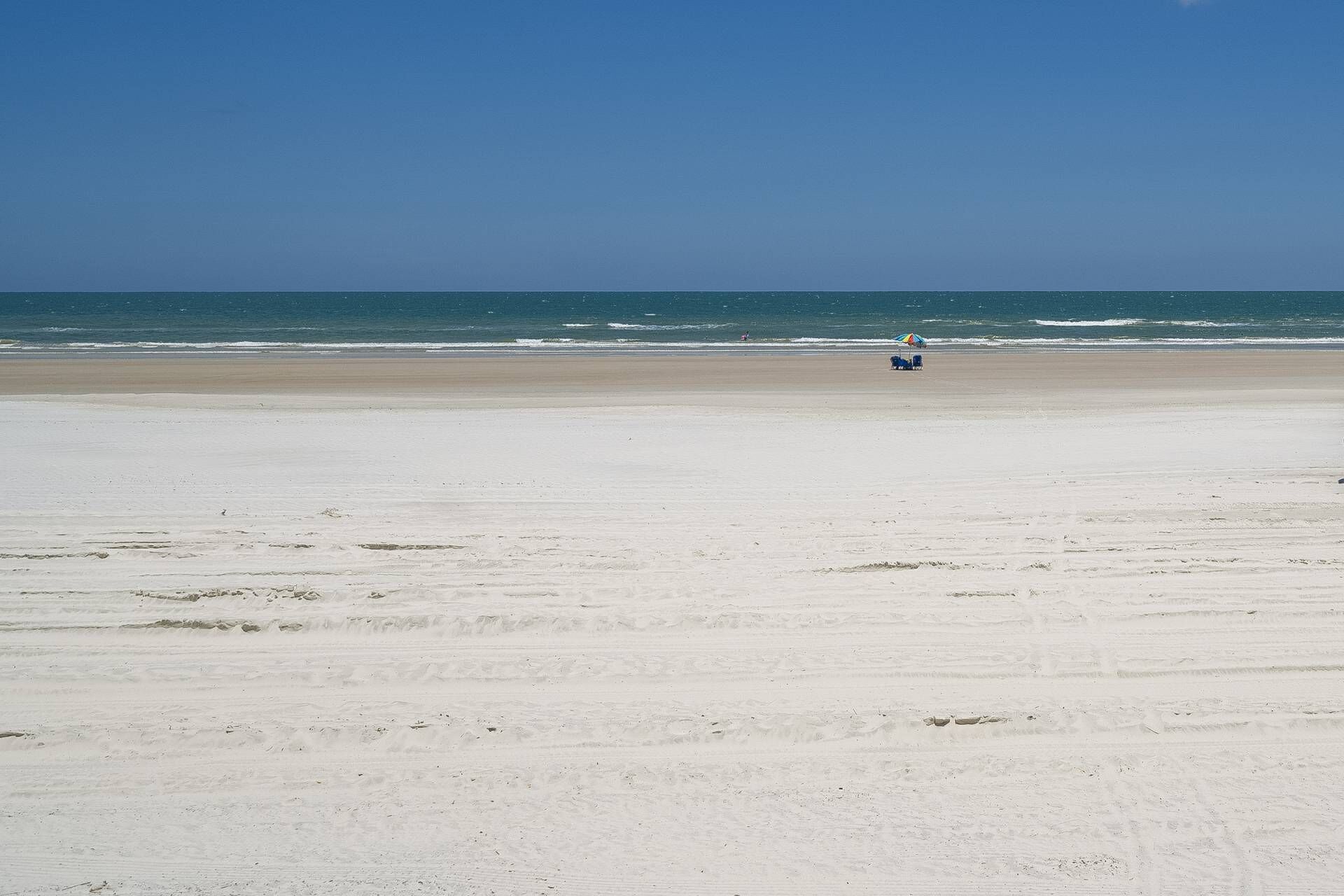 Een breed zandstrand met een helderblauwe lucht en een rustige zee.