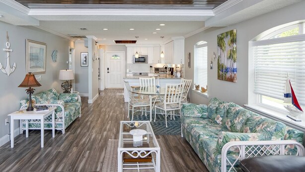 A spacious living area with a kitchen in the center, featuring a dining table and chairs, a sofa, and a coffee table. - Castillo del Sol (St. Augustine)