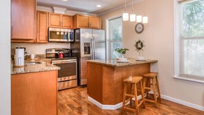 A modern kitchen with wooden cabinets, stainless steel appliances, a granite countertop, and a small island with stools. - Castillo Suite (St. Augustine)