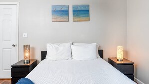 A bedroom with a bed, two nightstands, a door, and two wall art pieces. - Castillo Suite (St. Augustine)