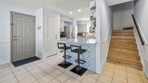 Une cuisine moderne avec un îlot central, deux tabourets de bar et un escalier en bois.
