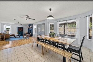 A spacious living room with a wooden dining table, black chairs, and a blue sofa. - Top-rated! Gated 4-acre with game room, XL SwimSpa, Fire pit (Leander)