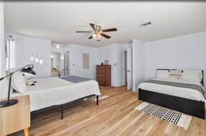 A bedroom with two beds, a ceiling fan, a desk with a lamp, and a patterned rug. - Top-rated! Gated 4-acre with game room, XL SwimSpa, Fire pit (Leander)