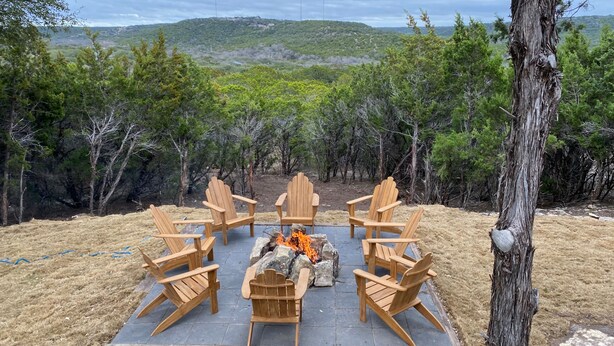 Un foyer entouré de chaises en bois, situé dans un cadre naturel et offrant une vue sur des collines lointaines.