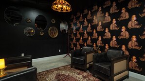 Ein Zimmer mit gestreifter Tapete, Ledersesseln, einem Kronleuchter und verschiedenen Wanddekorationen.