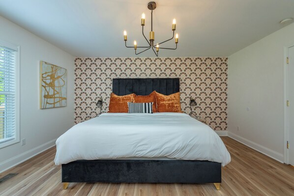 Une chambre à coucher avec un grand lit, un papier peint à motifs, un lustre et une fenêtre avec des stores.