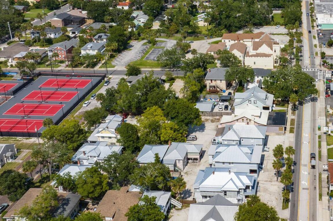 An aerial view of a residential area with houses, a tennis court, and a large building with a distinctive roof.