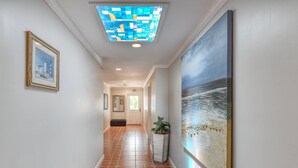 A hallway with a tiled floor, a framed picture on the left, a large painting on the right, and a ceiling light. - Anastasia Suite (St. Augustine)