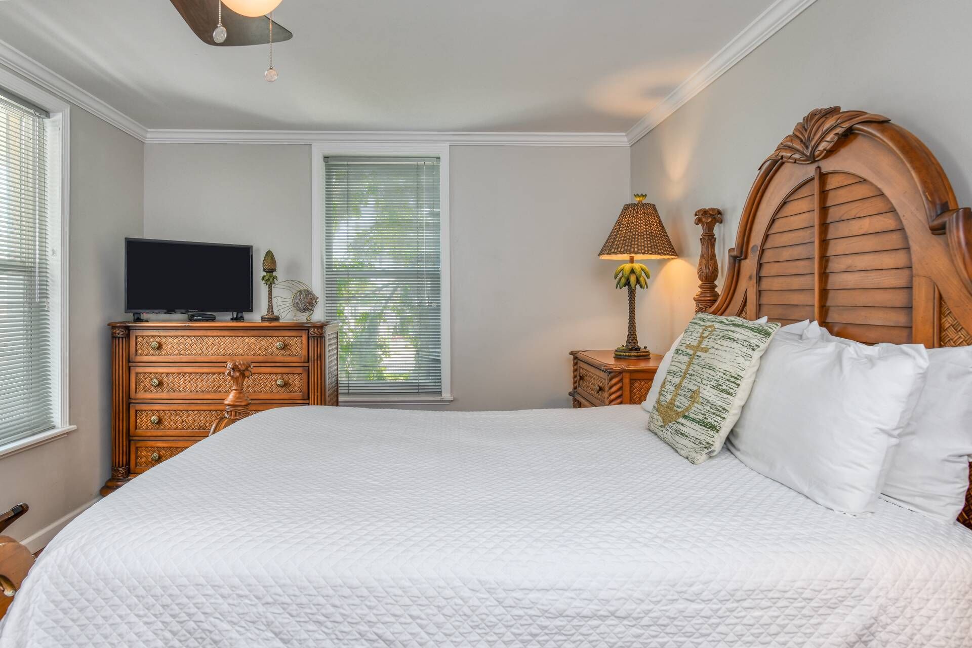 A bedroom with a large bed, a wooden dresser, a television, and a window with blinds.