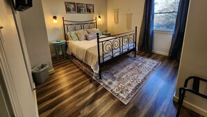 Een slaapkamer met een bed, een plafondventilator, een raam met gordijnen, een tafeltje en een aan de muur bevestigde televisie.