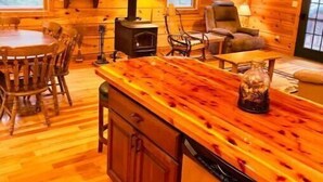Un accogliente interno di una baita con finiture in legno, una zona pranzo, una cucina con lavastoviglie e un camino.