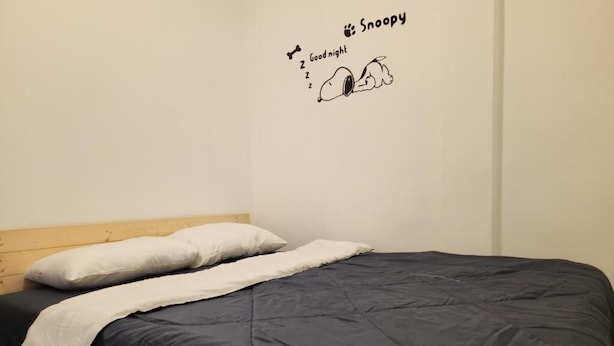 A single bed with a dark blue mattress and white pillows, a wooden headboard, and a wall decal with Snoopy and the text "Good night." - Jipu Homestay Ai Yoe Boe Chang (Betong)