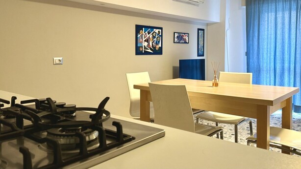 Een moderne keuken met een gasfornuis, een eettafel met stoelen en kunst aan de muur.