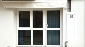 Een wit gebouw met dubbele glazen deuren, een klein hulpkasten en een bord met het nummer 10 aan de muur.