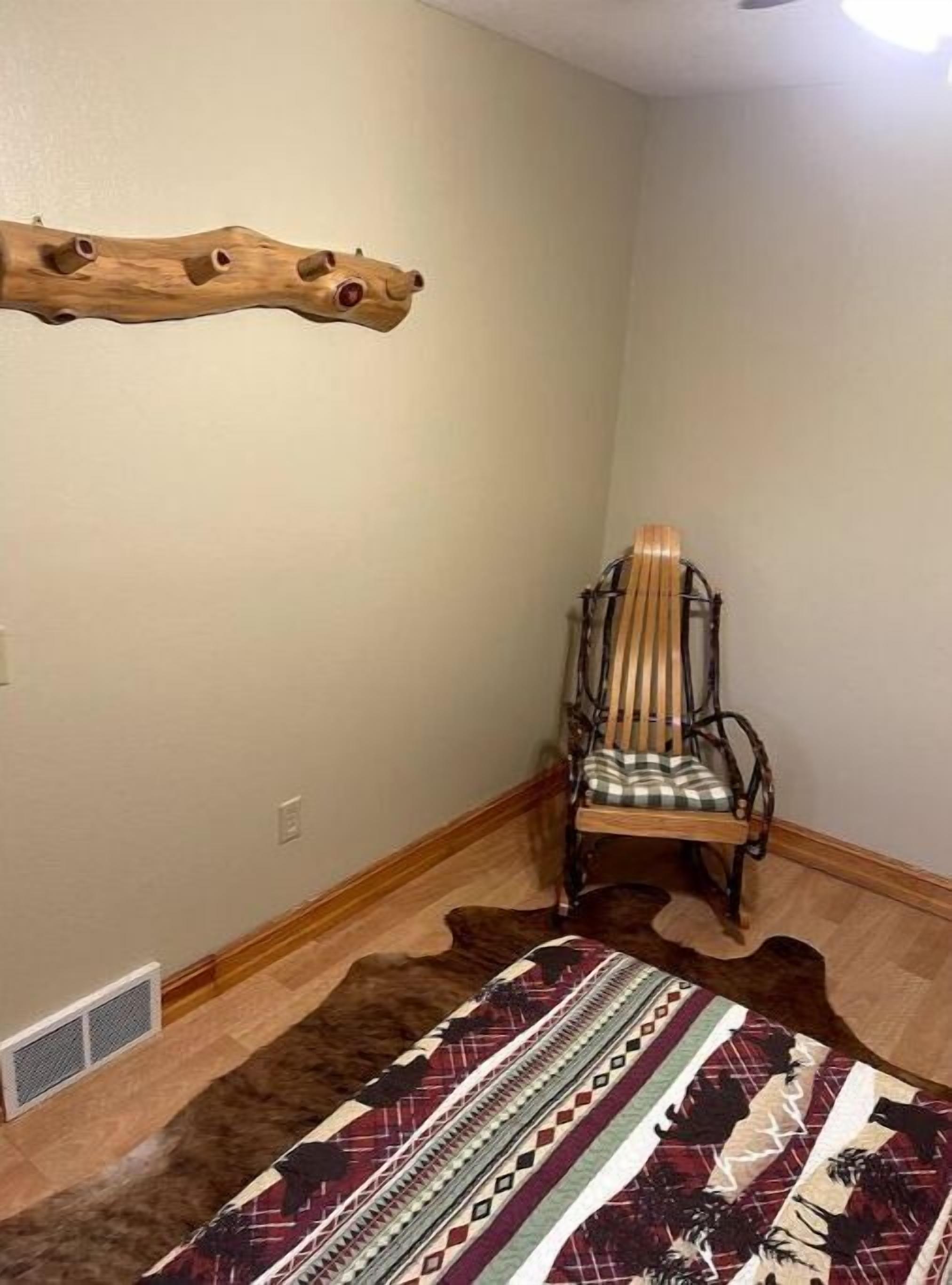 Une pièce d’angle avec une chaise en bois, un tapis à motifs et une étagère en bois fixée au mur.
