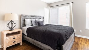 Ein Schlafzimmer mit einem Bett, einem Nachttisch mit Schubladen, einer Lampe und einem Fenster mit Jalousien.