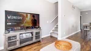 Ein modernes Wohnzimmer mit einem Flachbildfernseher, der eine Netflix-Serie zeigt, einer Holz-Unterhaltungsecke, einer Treppe und einer gemütlichen Sitzecke.