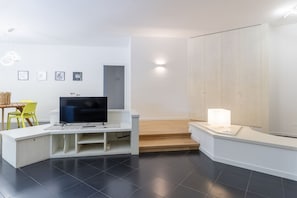Een moderne woonkamer met een flatscreen televisie, een witte tv-kast, een houten trap en een helder wandlamp.