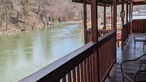 Eine Holzterrasse mit Geländer, die auf einen Fluss blickt, mit Bäumen und Hügeln im Hintergrund.