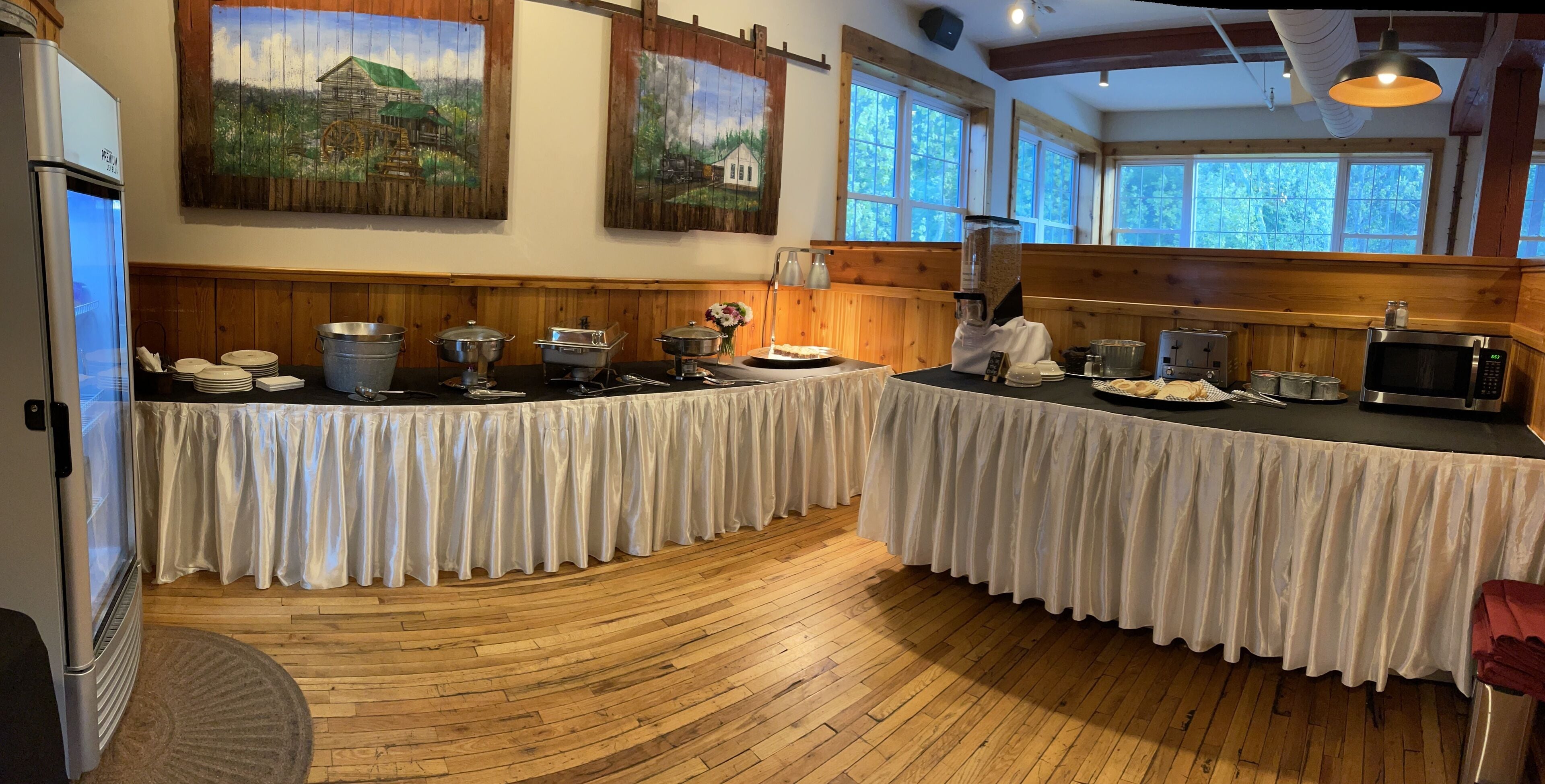 A buffet setup with two covered tables, a refrigerator, and a microwave.