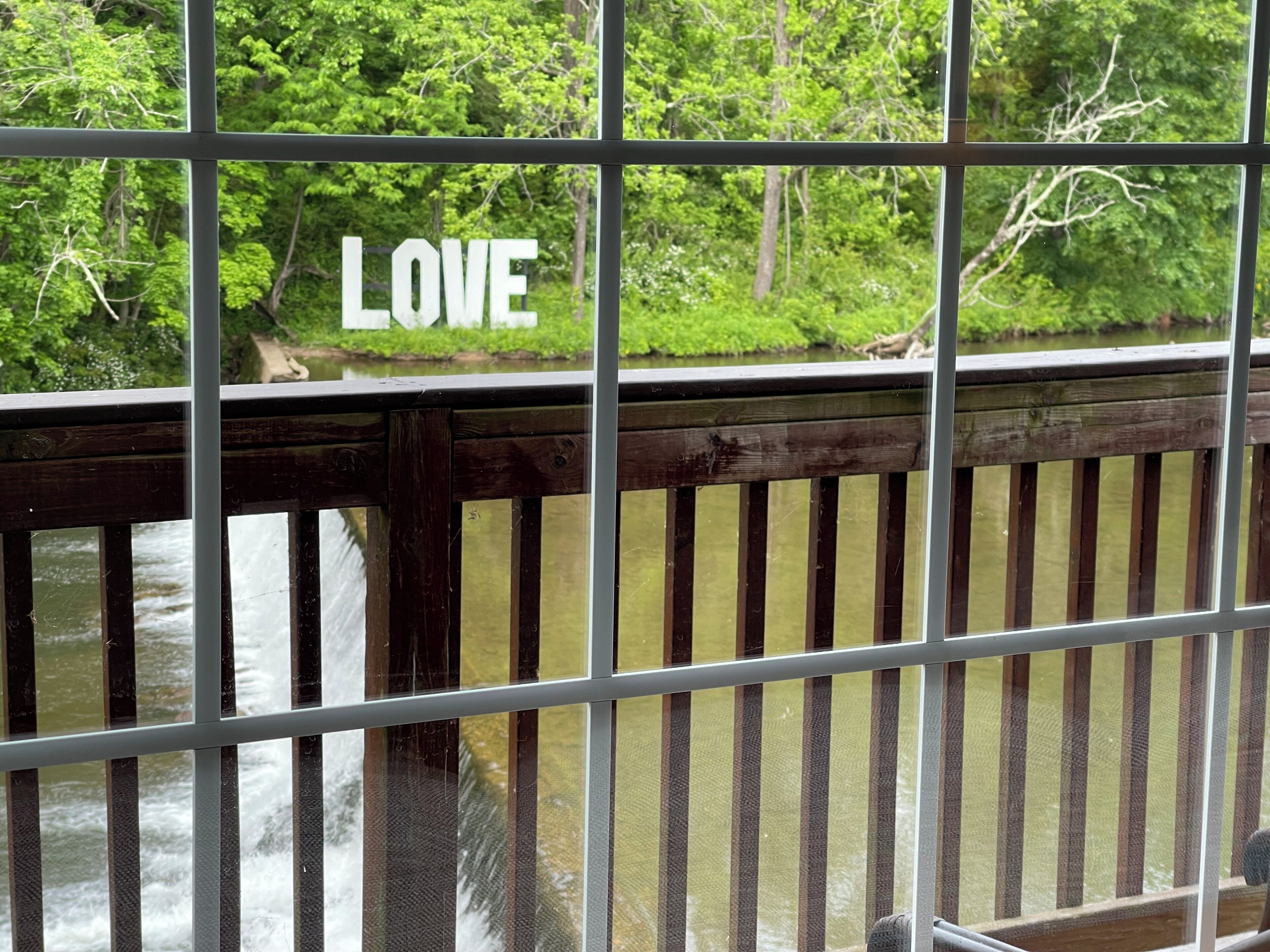 Une vue à travers une rambarde métallique sur laquelle on peut lire le mot « AMOUR », donnant sur une rivière et une végétation luxuriante.