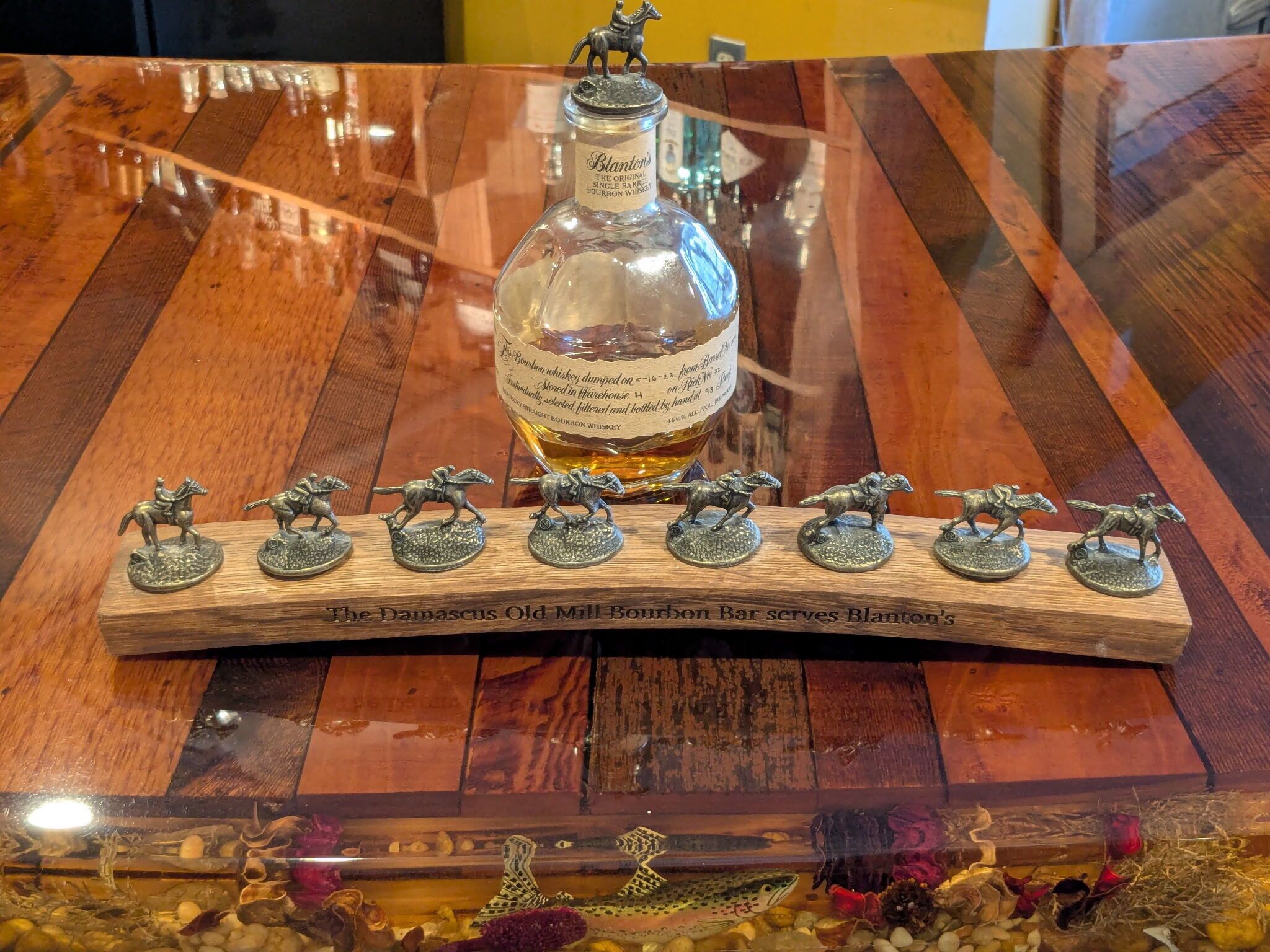 A wooden bar with a bottle of Blanton's bourbon whiskey and horse figurines.