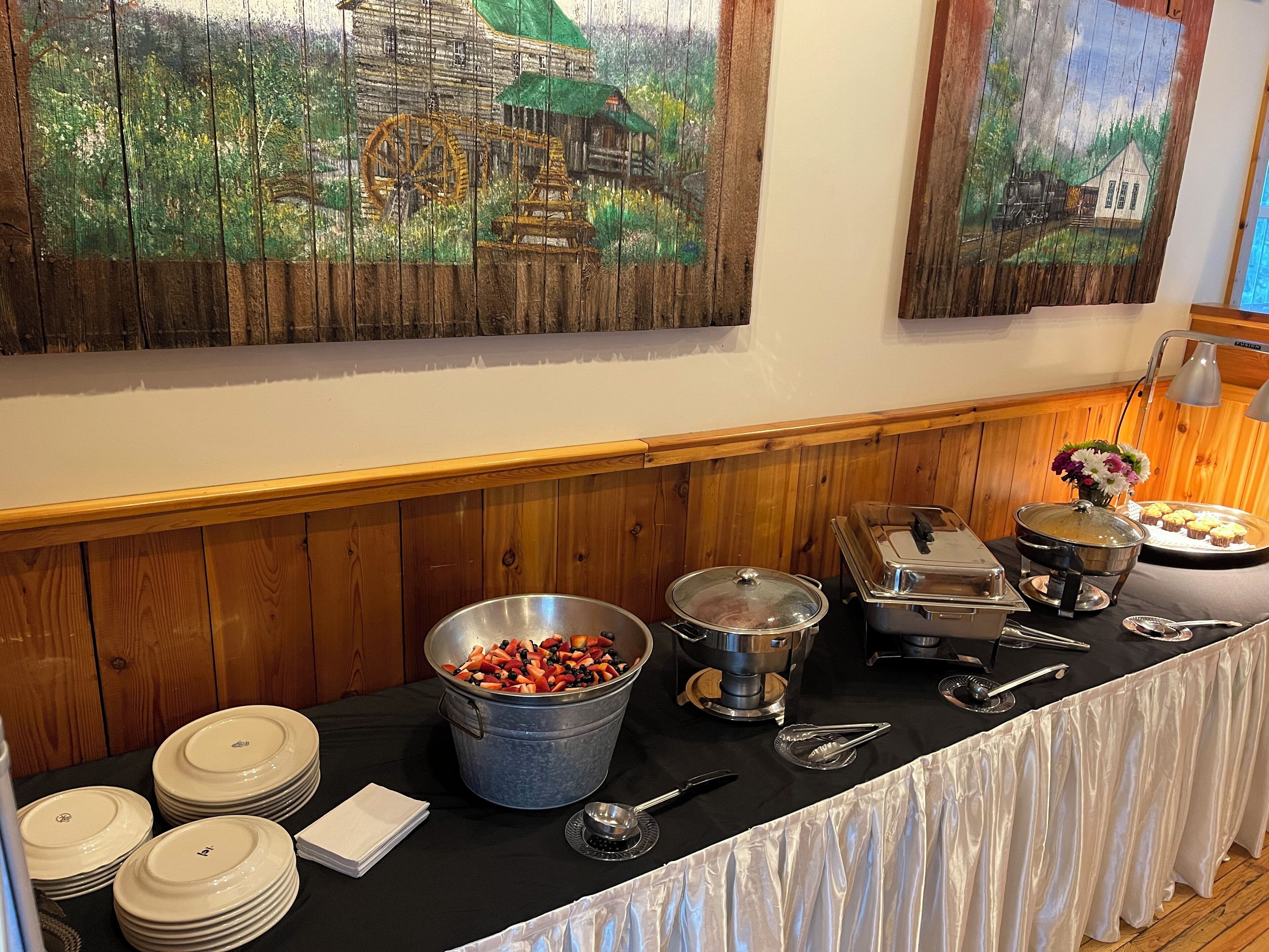 A buffet setup with various food containers, utensils, and a table covered with a black cloth.