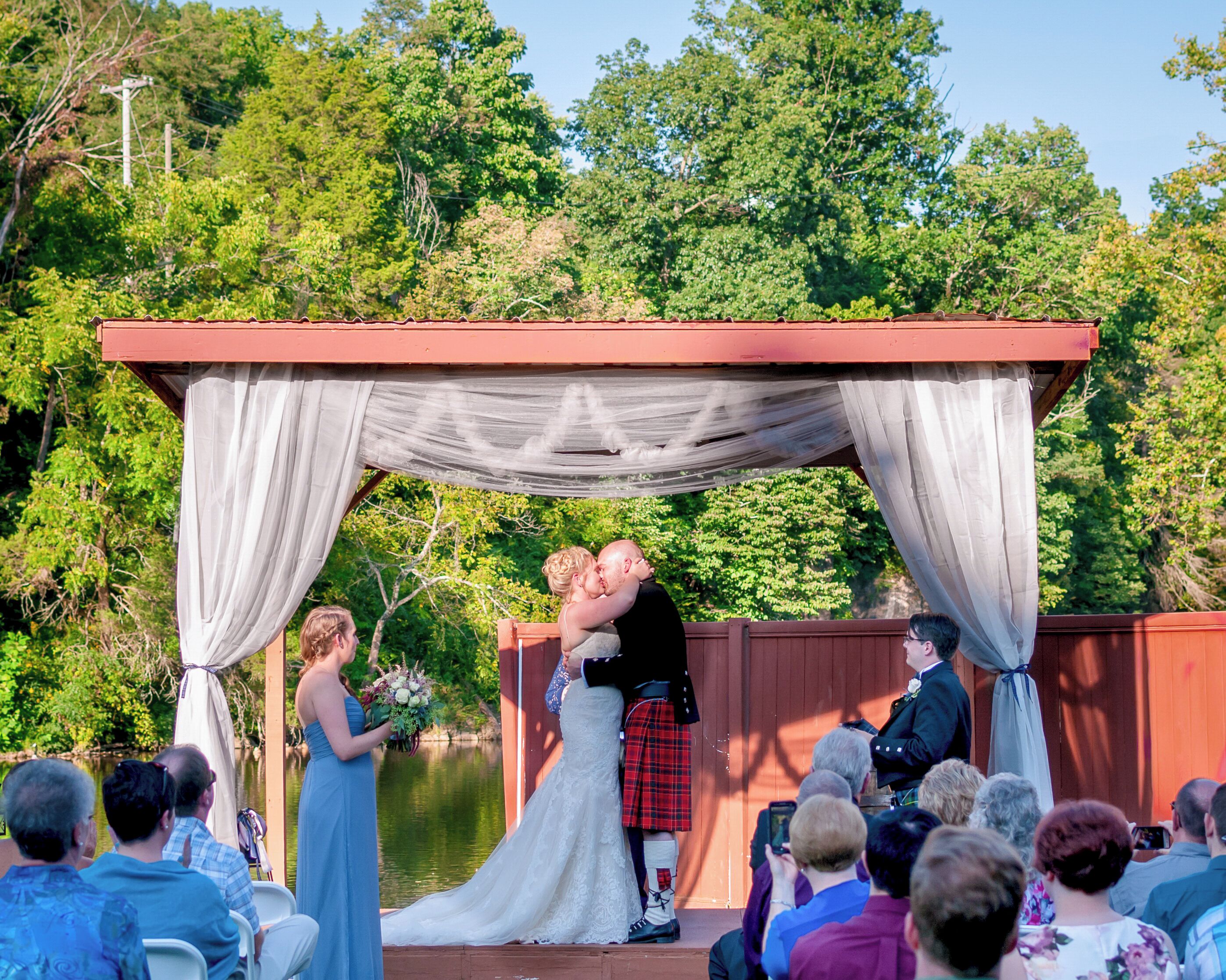A wedding ceremony with a couple kissing under a canopy. Guests are seated in rows facing the couple.