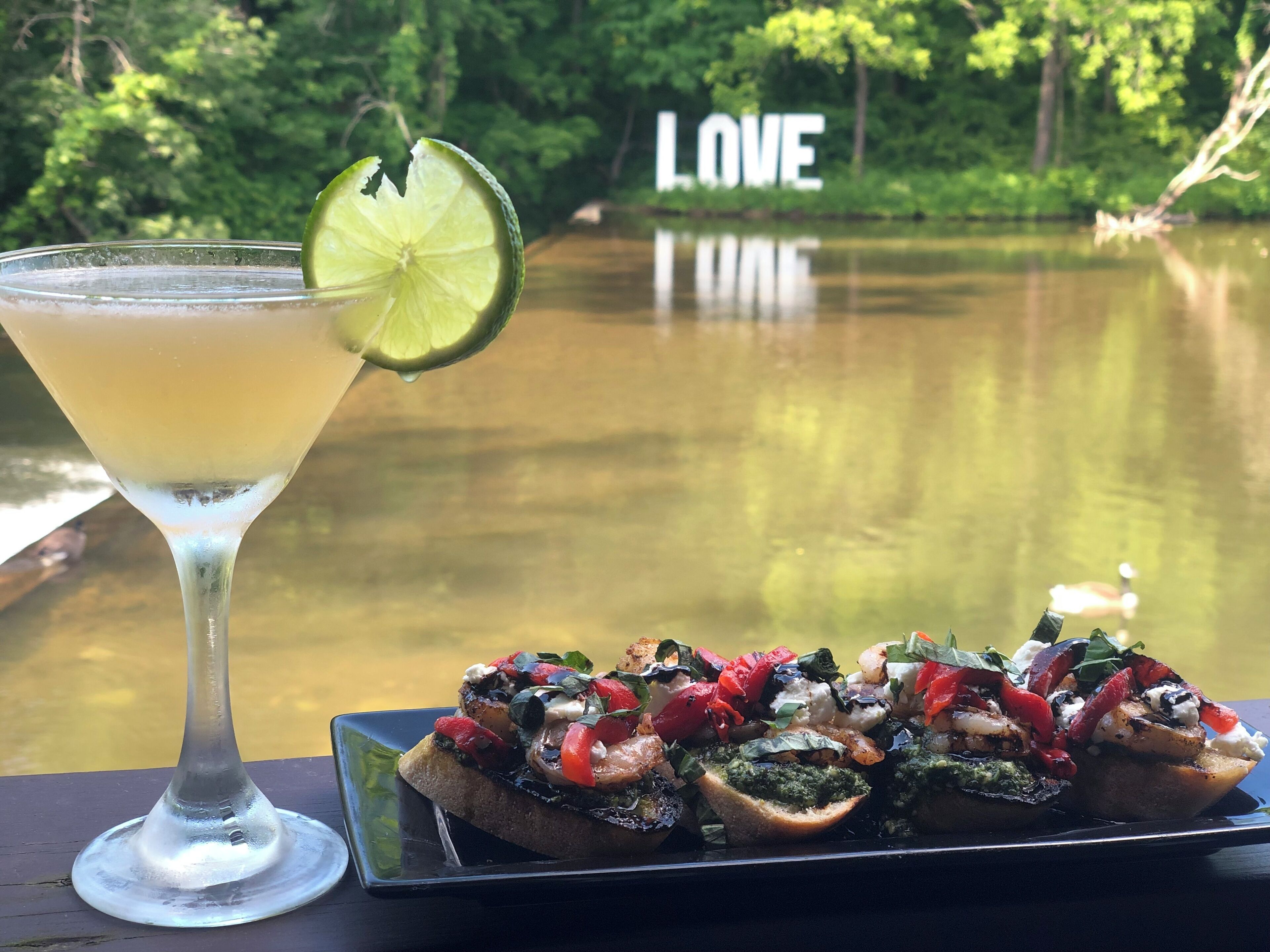 Un verre à martini garni d’une tranche de citron vert et une assiette de bruschettas garnies de divers ingrédients.