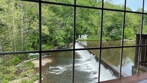 Blick durch ein Fenster mit Metallgitter auf einen Fluss mit Wasserfall und üppigem Grün.