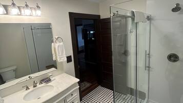 Un baño con lavamanos blanco, espejo y cabina de ducha de vidrio.