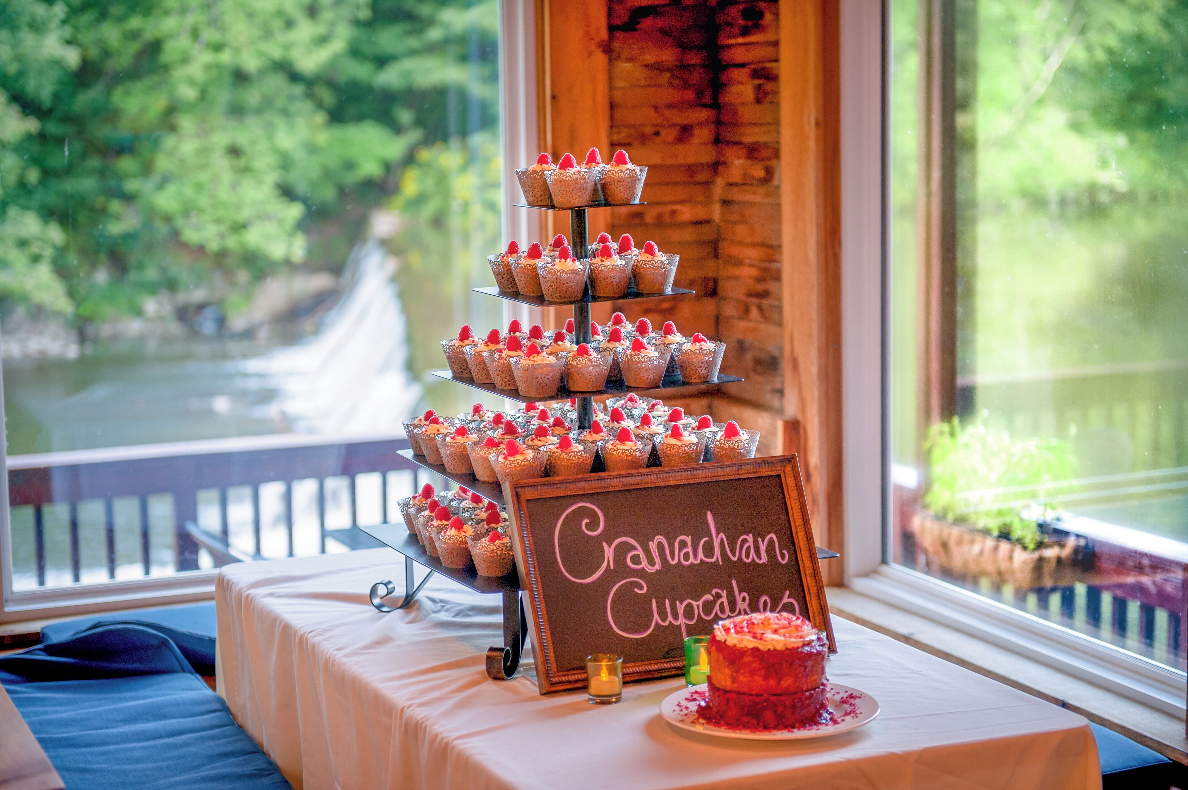 A tiered cupcake display with a sign reading "Granachan Cupcakes" on a table by a window with a view of greenery.