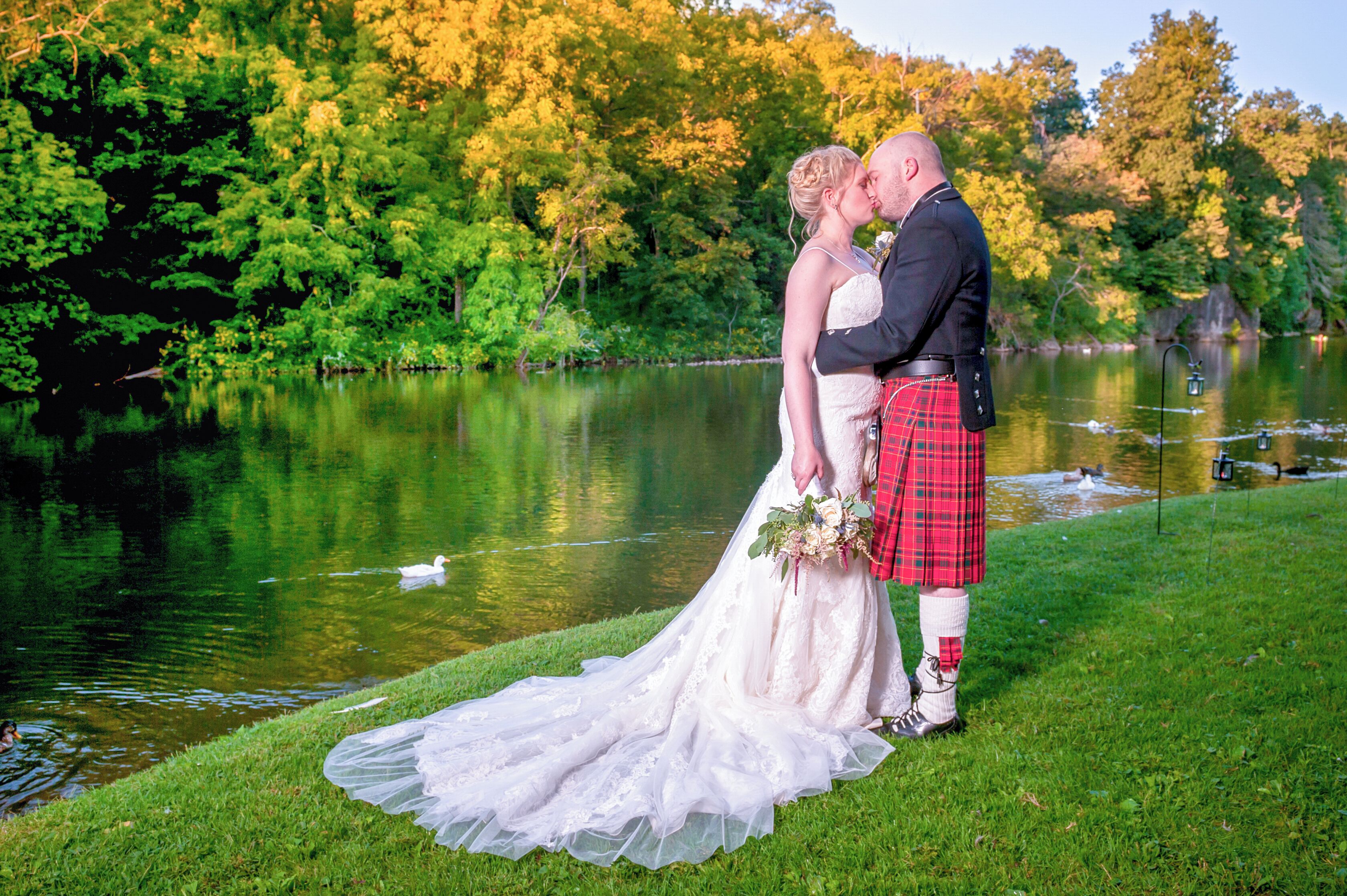Una pareja de novios junto a un lago, con un bote al fondo.