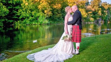 Una pareja de novios junto a un lago, con un bote al fondo.