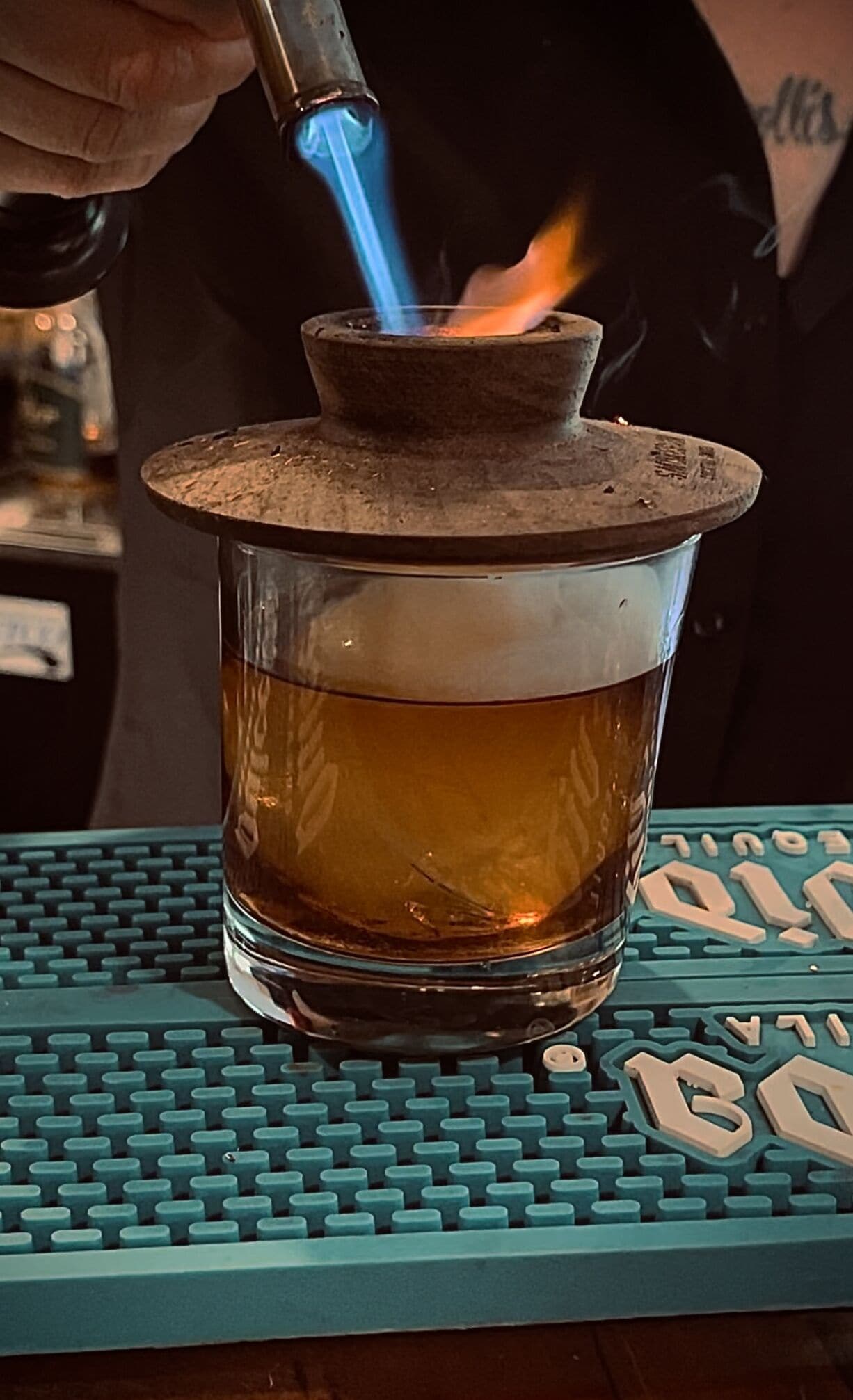 A glass of amber liquid on a teal coaster with a keyboard-like pattern.