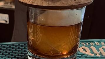 Un verre contenant un liquide ambré, posé sur un dessous de verre turquoise orné d’un motif rappelant un clavier.