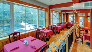 Ein Restaurant mit mehreren Tischen und Stühlen, großen Fenstern mit Blick auf einen Fluss und einer Holzinnenausstattung.