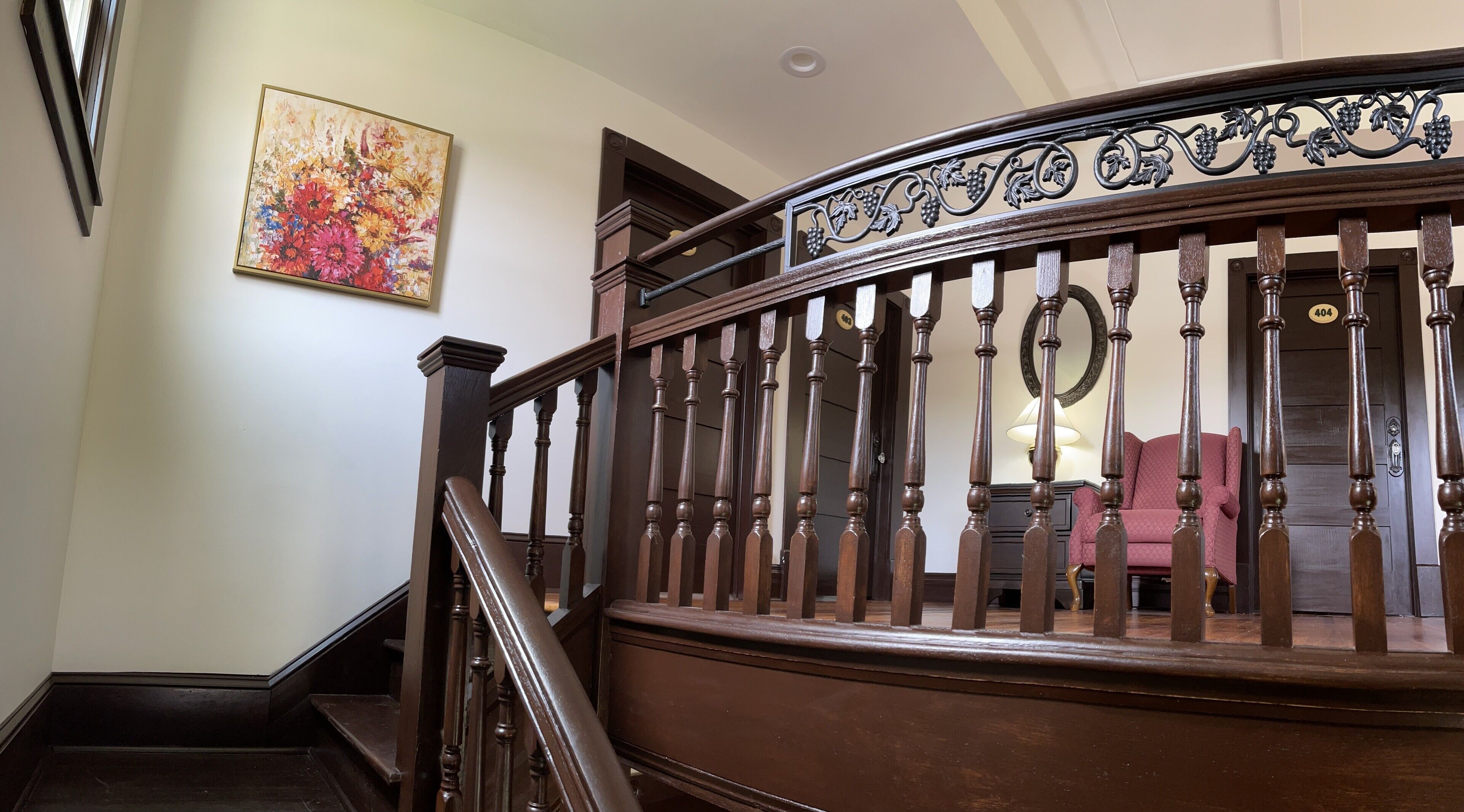 Una escalera de madera con barandilla decorativa y un cuadro floral en la pared.