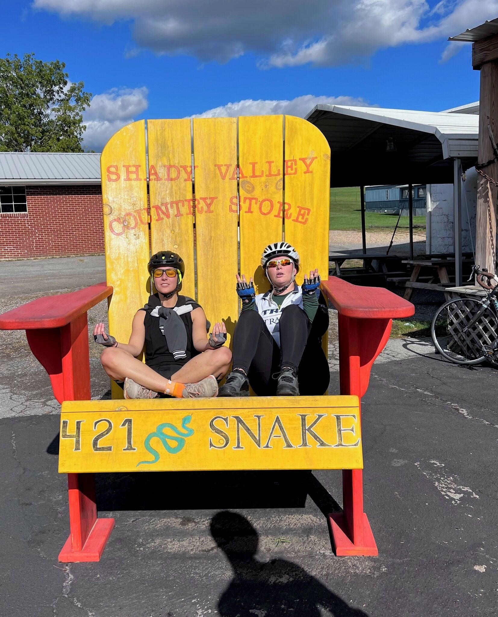 Dos personas sentadas en una silla de madera con la inscripción 'SHIELD VALLEY COUNTY STORE' y '421 & SNAKE'.
