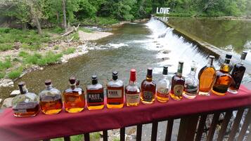 Une rangée de bouteilles de whisky sur une table rouge, près d’une rivière, avec une cascade en arrière-plan.