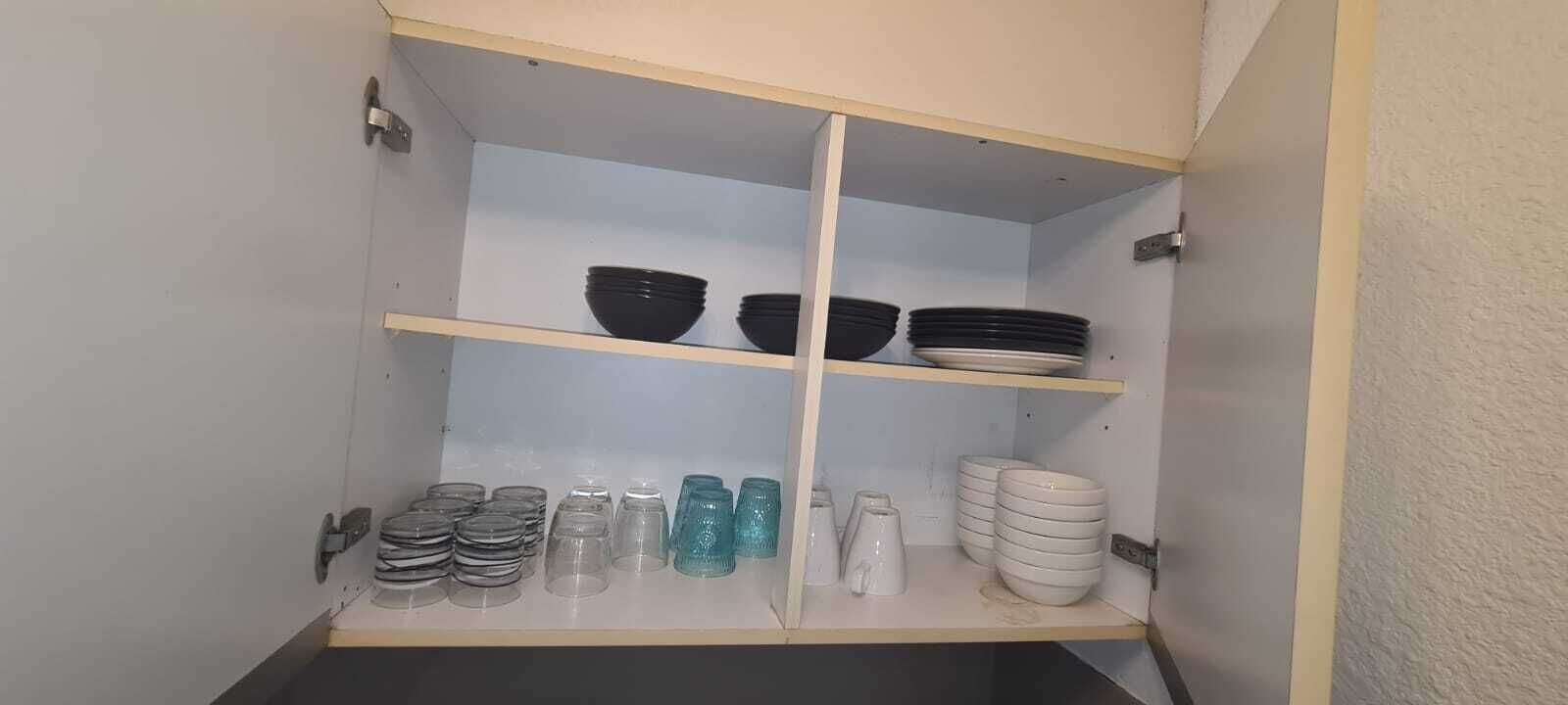 Keittiön yläkaappi, jossa on hyllyjä, ja hyllyillä mustia ja valkoisia kulhoja, lautasia ja lasiesineitä.