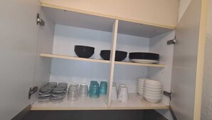 A kitchen cabinet with shelves containing black and white bowls, plates, and glassware.